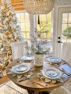 a dining room table with plates and silverware on it in front of a christmas tree