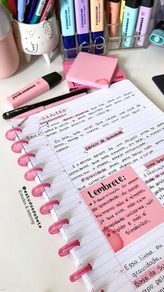 an open notebook with pink sticky notes and pens on it next to other office supplies