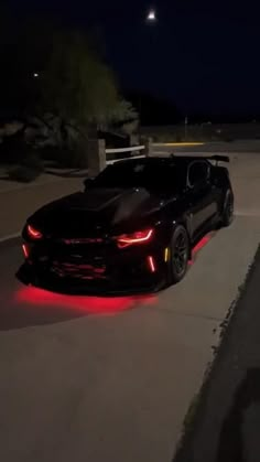 a black sports car with red lights on it's hood parked in a driveway