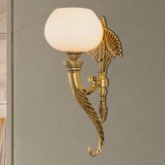 a wall light with a white glass shade on it's arm and an ornate brass finish