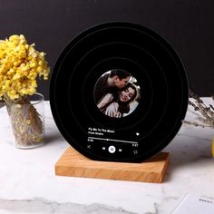 a black clock with a photo on it next to some yellow flowers and vases