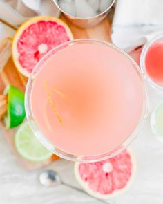 a pink drink in a glass next to sliced grapefruit