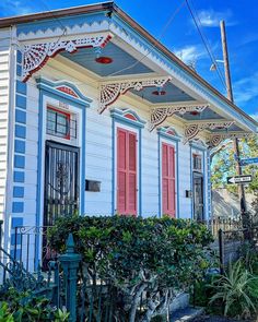 a white house with red shutters and green bushes on the front porch, next to a fence