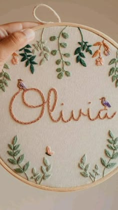 someone is stitching an embroidered name on a piece of fabric with leaves and flowers