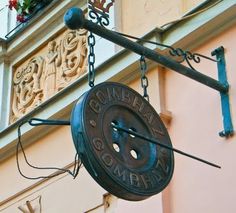 a sign hanging from the side of a building with flowers growing out of it's windows