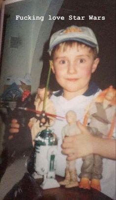 a young boy holding a star wars toy in his right hand while wearing a hat