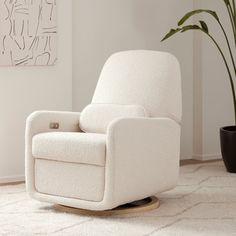 a white rocking chair sitting on top of a rug next to a potted plant