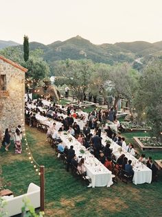 a group of people sitting at long tables in the middle of a field with lights on them