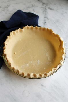 an uncooked pie crust sits on a marble countertop next to a blue napkin