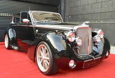 an antique black car is parked in front of a garage door on a red carpet