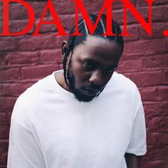 a man with dreadlocks standing in front of a red brick wall and wearing a white t - shirt