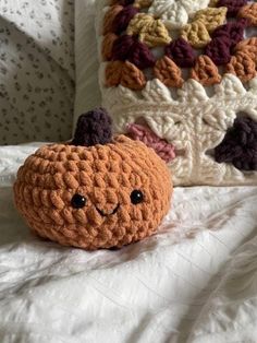 a small crocheted pumpkin sitting on top of a bed next to a pillow