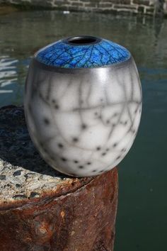 a blue and white vase sitting on top of a wooden post next to the water