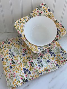 two place mats with flowers on them are next to a white bowl and plate in front of a wall