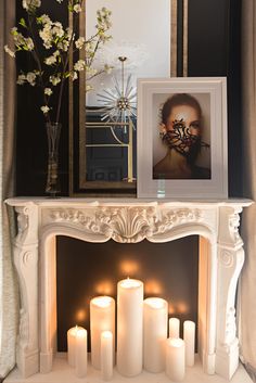 a white fireplace with candles on it in front of a mirror and framed photograph over the mantel