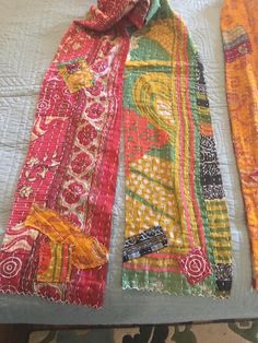 three different colored ties laying on top of a white bed sheet covered in colorful fabric