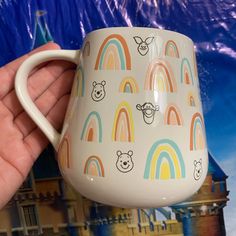 a hand holding a coffee mug in front of a castle with rainbows and bears on it