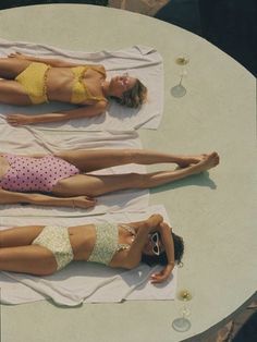 two women in bikinis are laying on towels