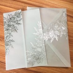 three envelopes with floral designs on them sitting on a wooden table next to each other