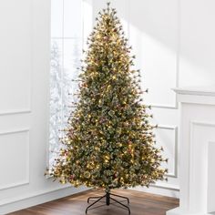 a small christmas tree in a room with white walls and wooden floors, decorated with multi - colored lights