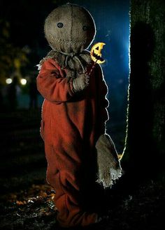 a creepy doll holding a yellow object in his hand and standing next to a tree at night