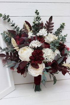 a bridal bouquet with red and white flowers, greenery and leaves on the side of a building