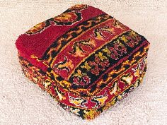 a multicolored ottoman sitting on top of a white floor next to a rug