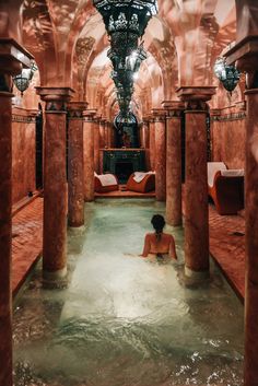 a woman is sitting in the middle of a large indoor swimming pool that has columns on both sides