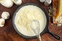 a pan filled with cheese on top of a wooden table next to garlic and other ingredients