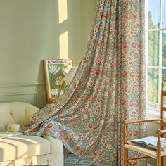 a living room with a large window covered by a floral drape and chair in front of it