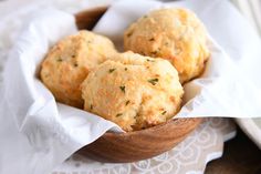 three biscuits are in a wooden bowl on a lace doily with a spoon and napkin