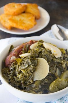 a bowl filled with green vegetables next to some fried food on a plate and silverware