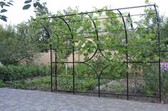 an iron trellis with vines growing on it's sides near a brick walkway