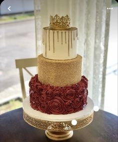 a three tiered cake with gold and red frosting on the top is sitting on a table