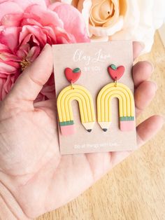 a person holding a card with some type of earring on it and flowers in the background