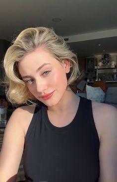 a woman with blonde hair and blue eyes wearing a black top sitting in front of a couch