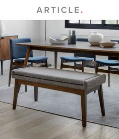 a dining room table with blue chairs and a bench in front of it that says article