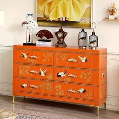 an orange dresser with birds and flowers painted on the drawers is in front of a painting