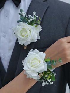 two white roses and greenery are on the arm of a man in a tuxedo