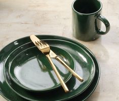 a green plate with two gold forks on it next to a cup and saucer