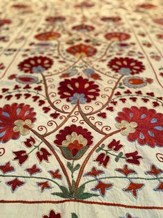 an embroidered table cloth with red and blue flowers on the border, sitting on top of a bed