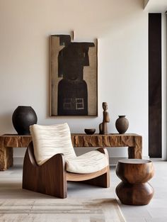 a chair and table in a room with art on the wall behind it, along with vases