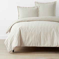 a bed with white and beige striped comforter set on top of wooden flooring