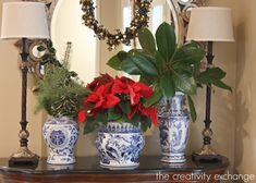 three blue and white vases with poinsettias on a table in front of a mirror