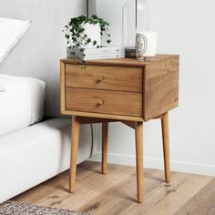 a bedside table with two drawers and a plant on it next to a white couch