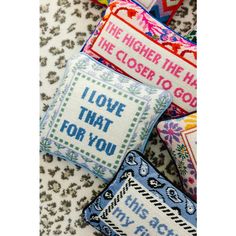 four cross stitch pillows sitting on top of each other with words written in different colors