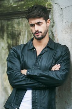 a young man with his arms crossed leaning against a wall wearing a black leather jacket