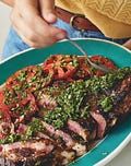 a person is cutting up some meat on a blue plate with red and green toppings