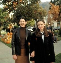 two women standing next to each other in front of some pumpkins on the ground