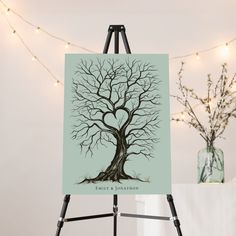 an easel with a tree on it next to a string of lights and a vase